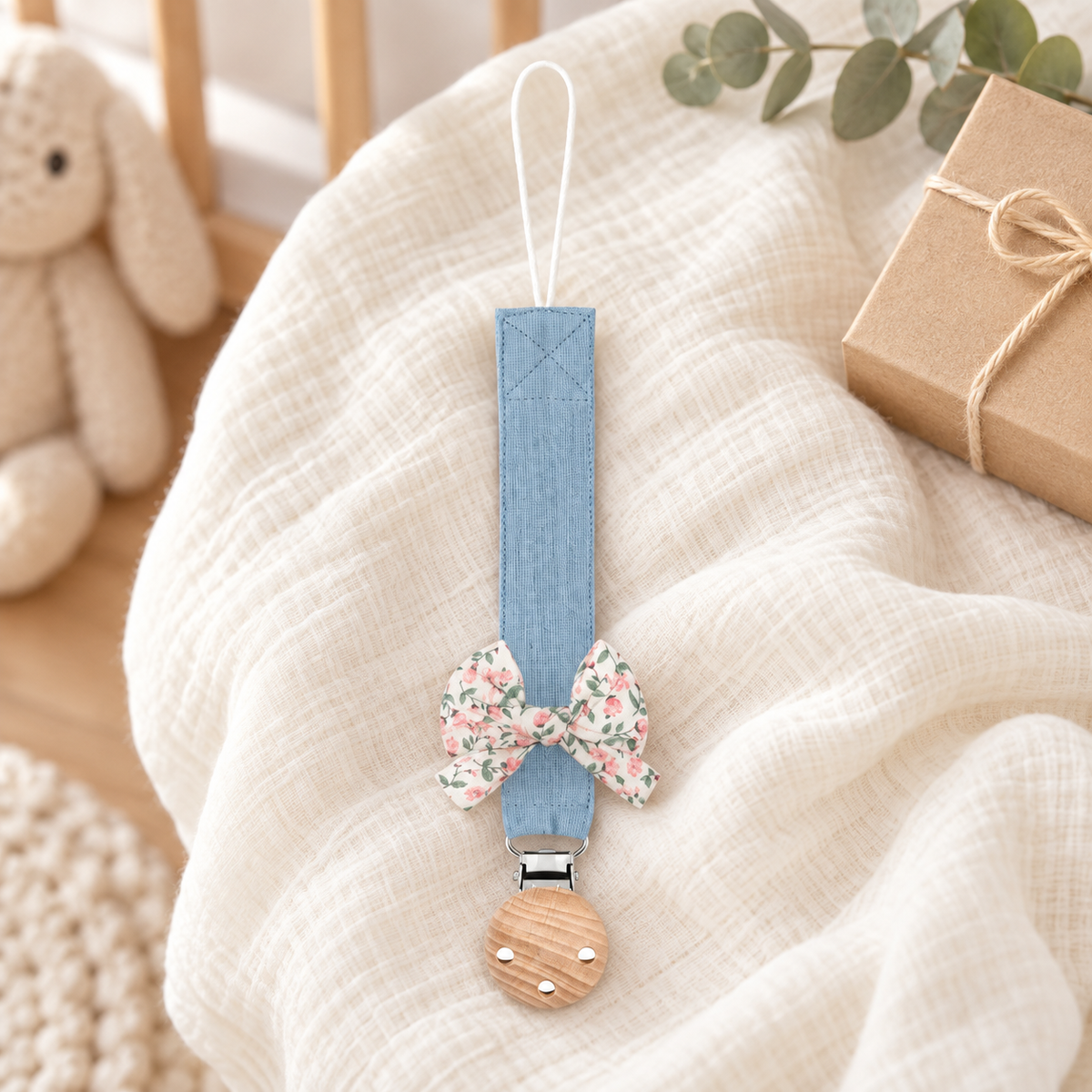Attache-tétine en tissu bleu ciel avec nœud fleuri et pince en bois